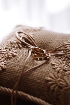 Rustic burlap cushion adorned with rings, showcasing wedding elegance and craft.
