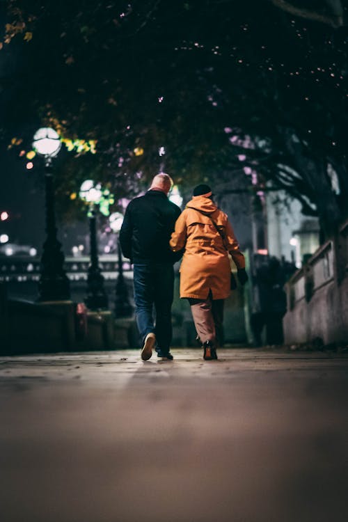 Back View of a Couple Walking on a Sidewalk in City at Night 