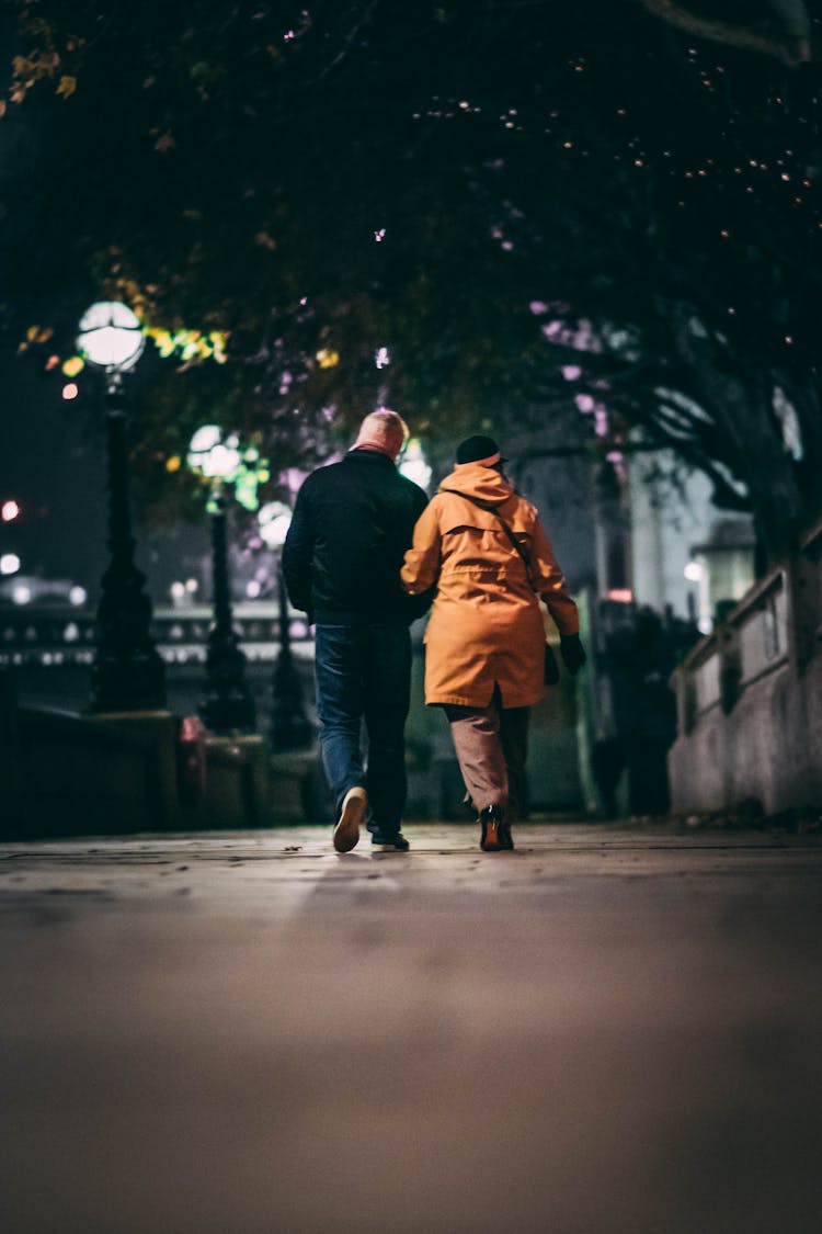 Back View Of A Couple Walking On A Sidewalk In City At Night 