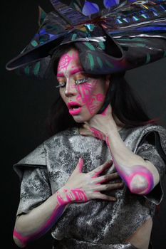 A woman in fantasy costume with vivid body paint and an elaborate headpiece poses dramatically.