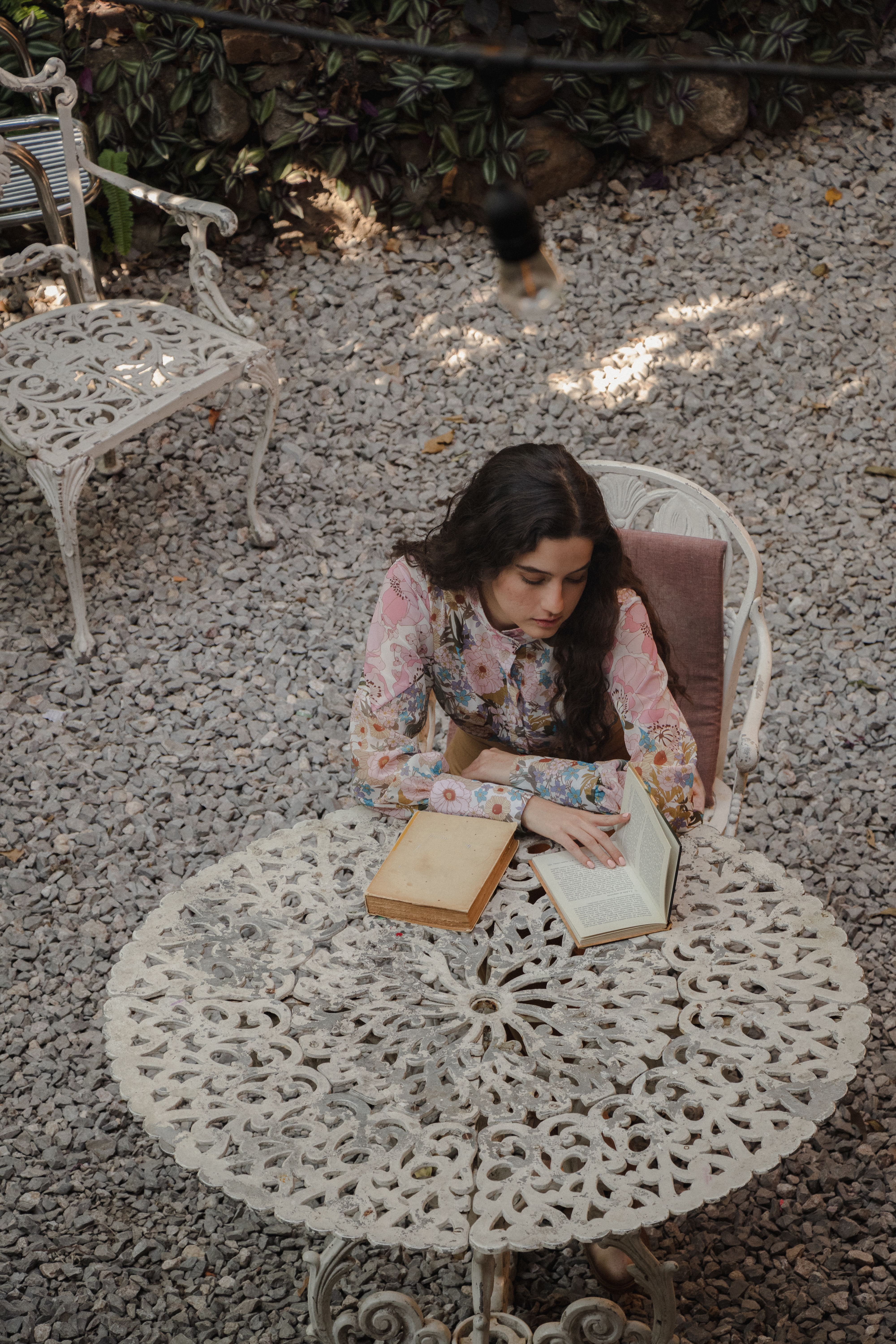 A woman reads at a vintage table in a garden setting, offering a serene moment.