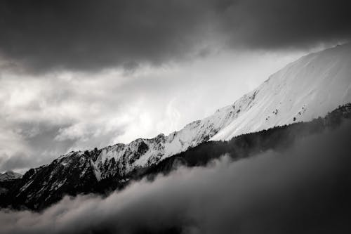 Grayscale Photo of a Snow Capped Mountain Under Cloudy Sky