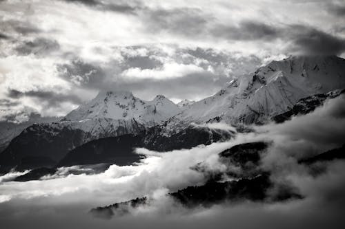 Grayscale Photo of a Snow Capped Mountains Under Cloudy Sky
