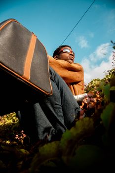 A fashionable man with sunglasses and a bag in a low angle view with a clear sky backdrop.