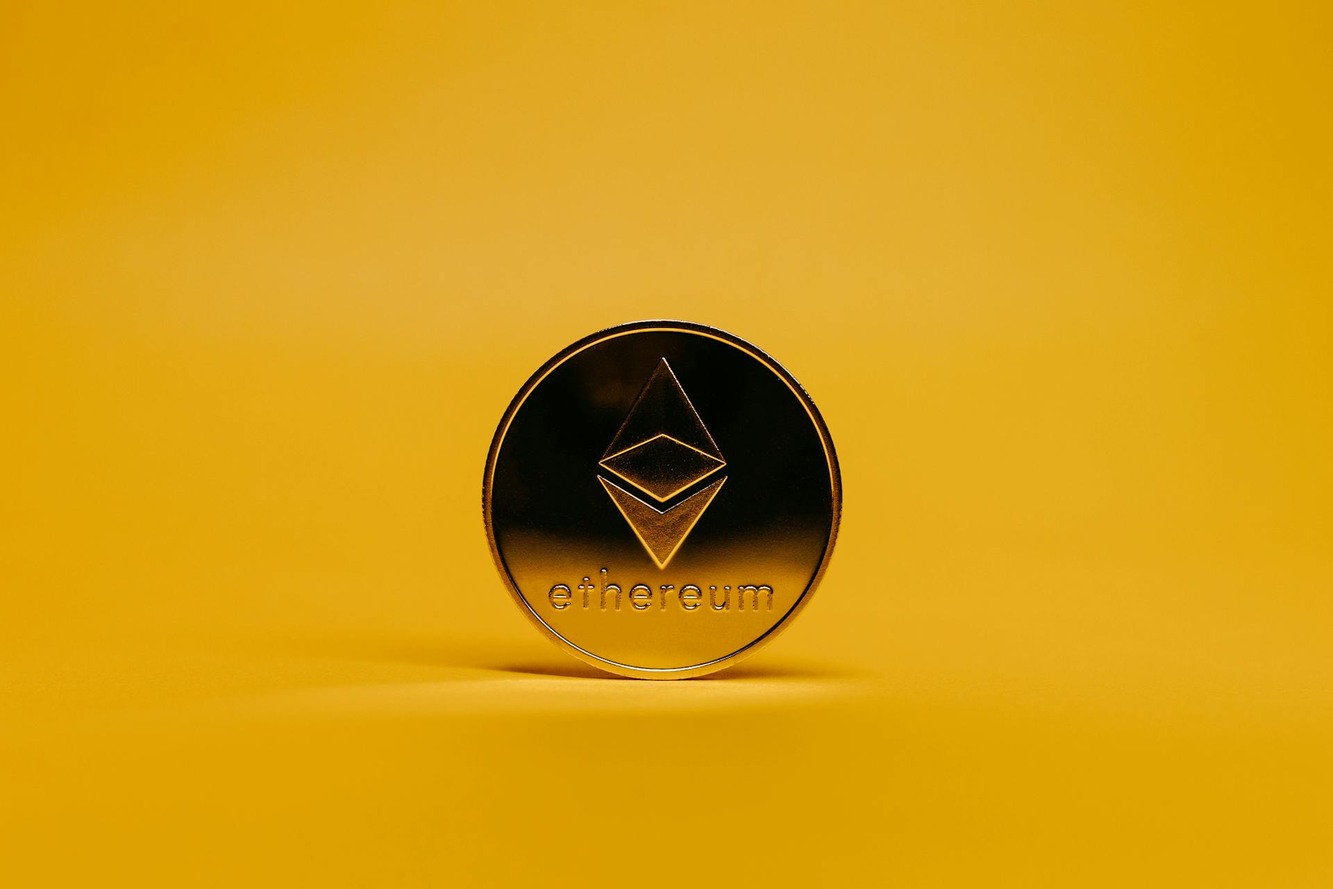 A shiny Ethereum coin displayed on a vibrant yellow background, symbolizing cryptocurrency.