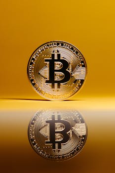 A golden Bitcoin coin reflects on a surface against a vibrant yellow background, symbolizing cryptocurrency.
