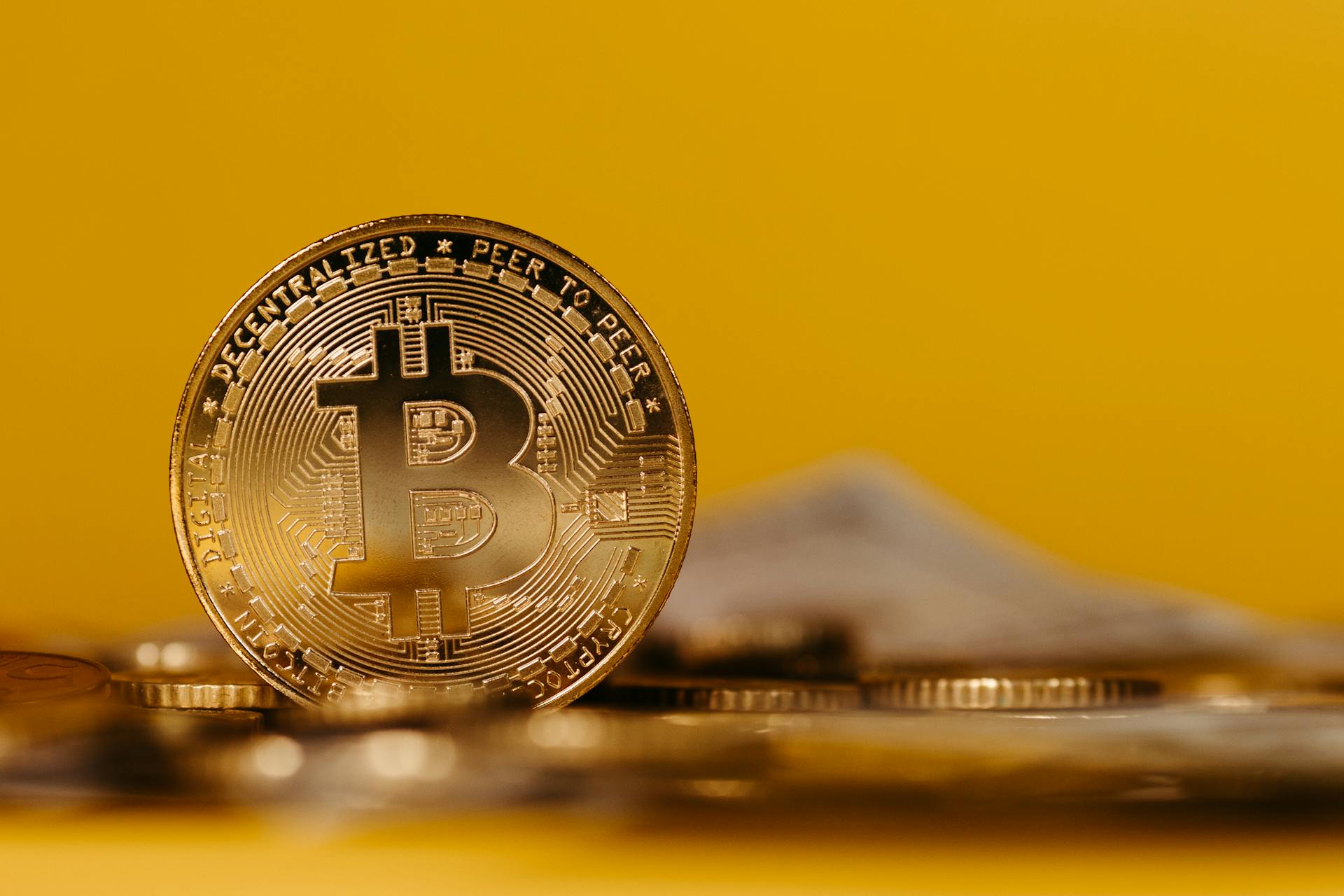 Detailed close-up image of a Bitcoin coin showcasing cryptocurrency with a bright yellow background.