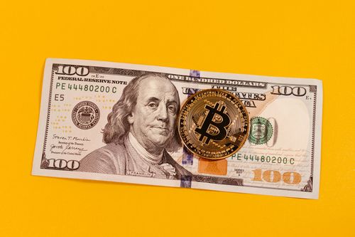 Free Gold bitcoin placed on a 100 US dollar bill over a bright yellow backdrop, symbolizing modern digital currency. Stock Photo
