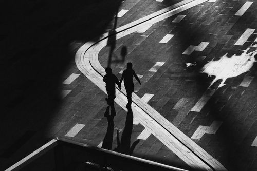 Free Artistic black and white silhouette of children holding hands and walking, highlighting shadows and light play. Stock Photo