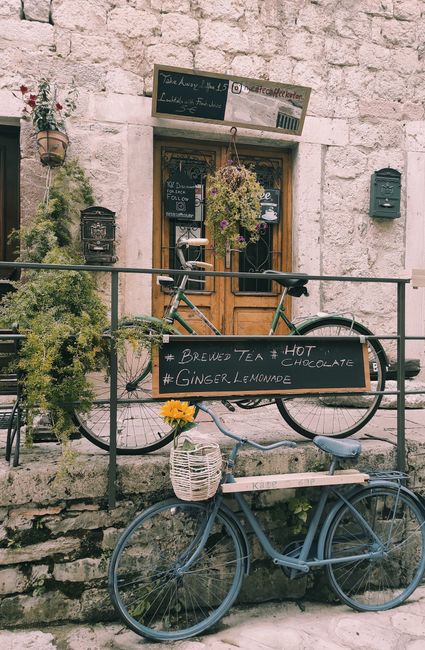 A quaint café in Kotor, Montenegro, featuring bicycles and a rustic stone wall. Perfect for capturing European charm.