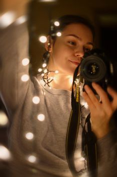 A woman taking a selfie with Christmas lights wrapped around her, capturing a cozy and festive mood.