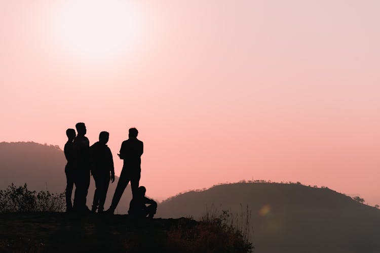 Silhouette Of Four People Standing On A Mountain