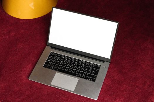 Mockup of a modern laptop with an open blank screen placed on a rich burgundy carpet.