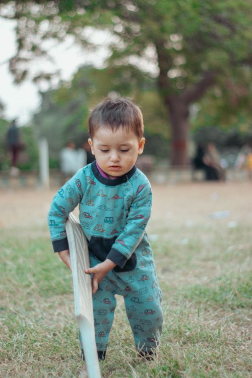 Free A toddler in pajamas playing with a plank outdoors on a grassy field. Stock Photo