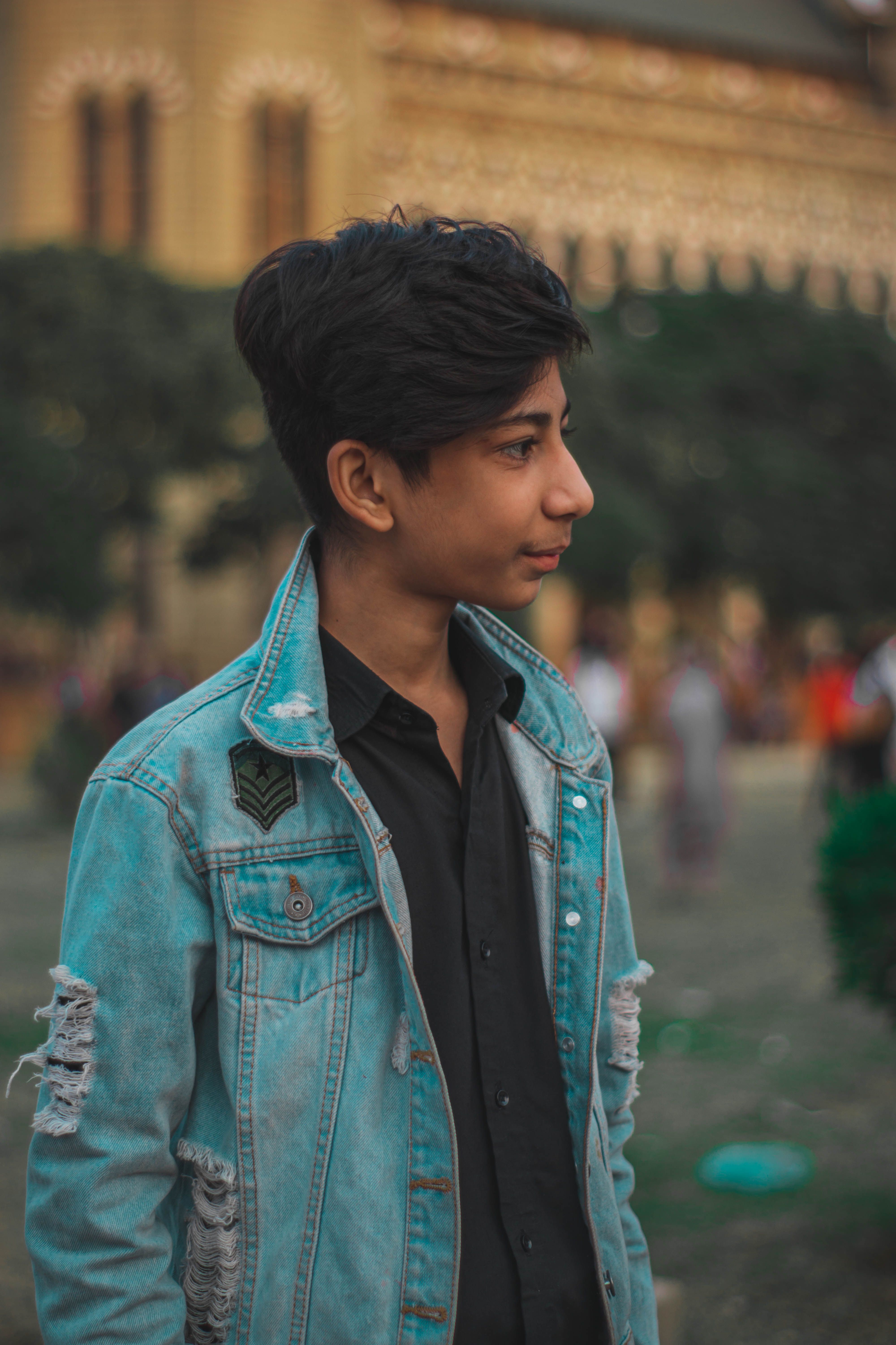 A stylish teenage boy in a denim jacket stands outdoors, exuding confidence and youth.
