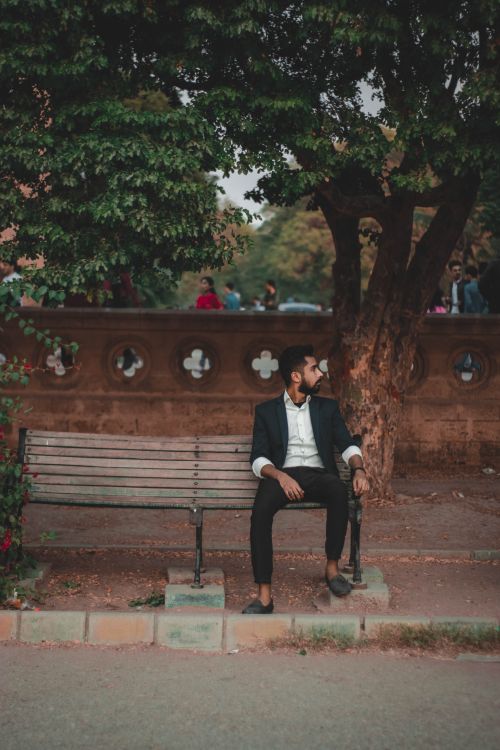 Free A man in a stylish suit sits alone on a park bench, looking contemplative. Stock Photo