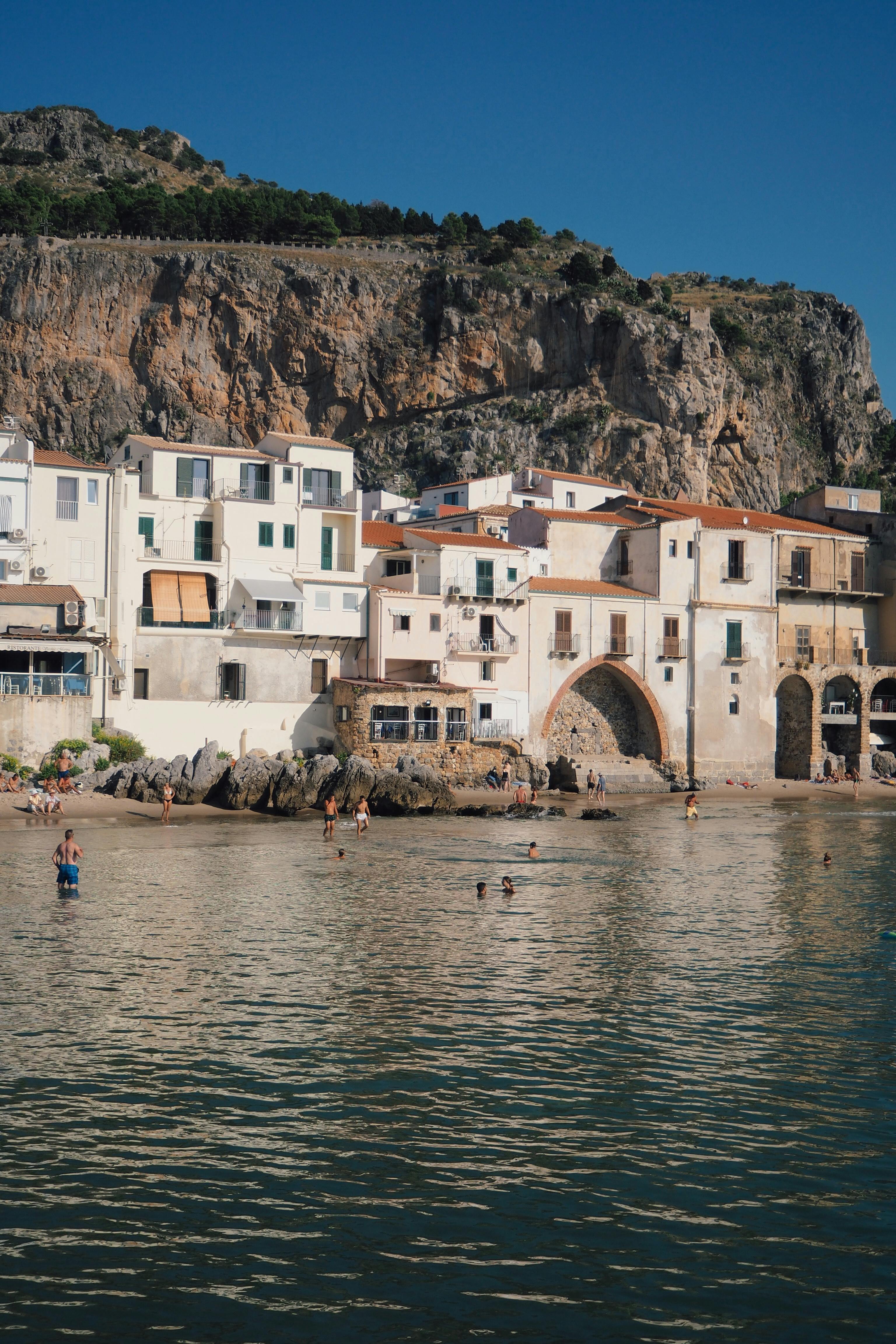 Picturesque coastal village with historic buildings against rocky cliffs, perfect for summer travel inspiration.