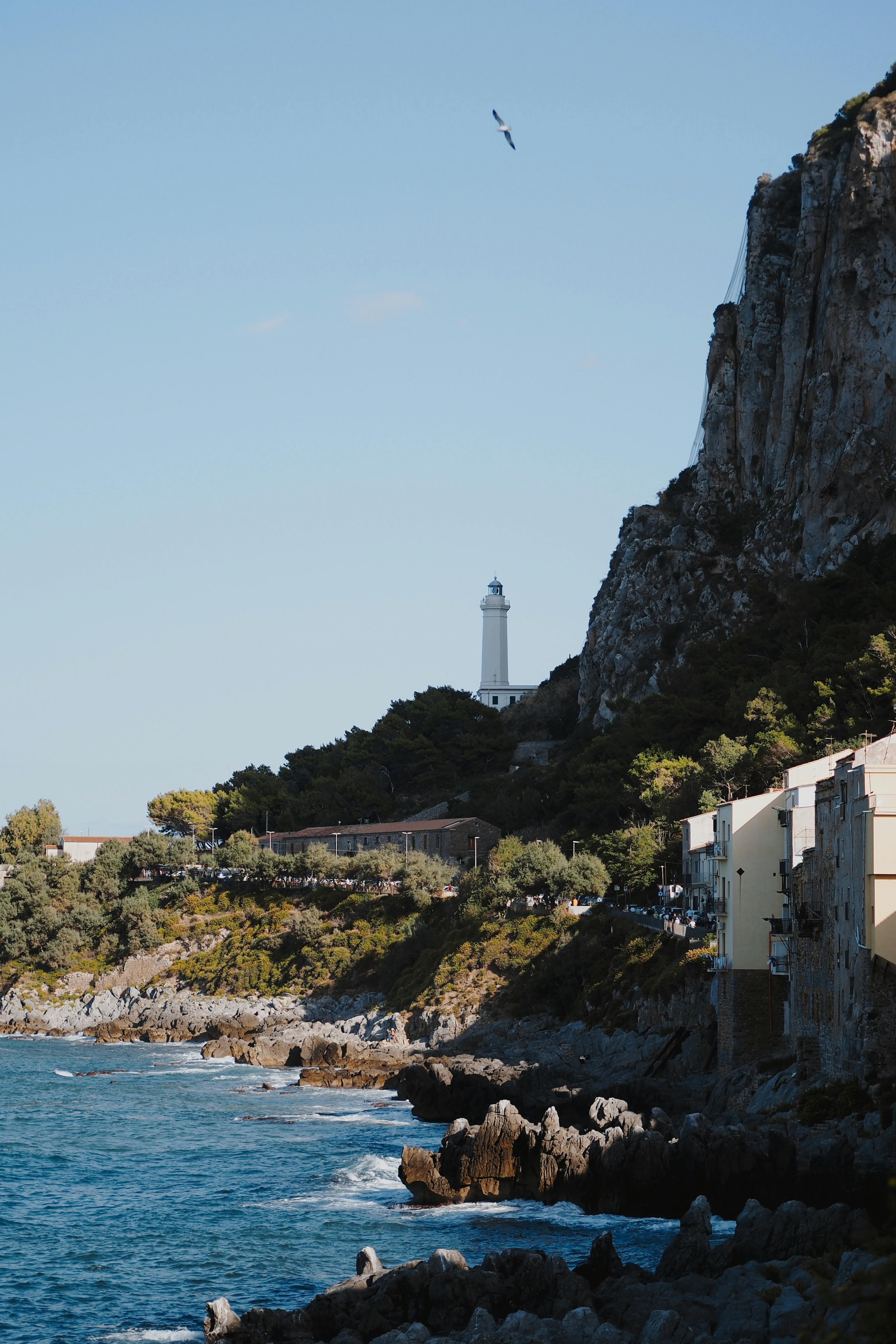 Scenic view of a lighthouse on a rocky coastline under a clear blue sky.