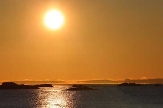 Silhouetted islands and sun reflecting on ocean during a vivid yellow sunrise.