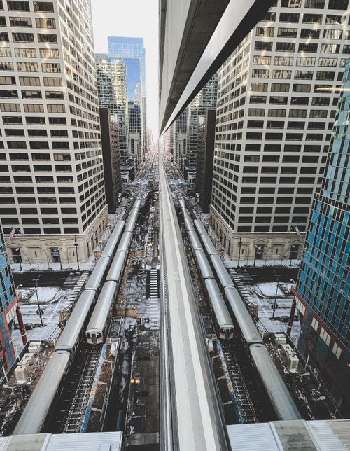 Free Aerial view of a city street with train tracks flanked by tall modern buildings. Stock Photo