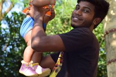 Man joyfully lifting a baby outdoors, surrounded by lush green foliage on a sunny day.