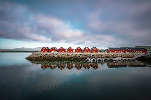 Idyllic view of red cabins reflecting in calm coastal waters in Norway at dawn.