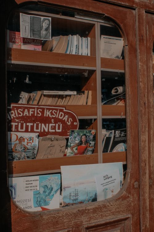 Free A diverse collection of books and magazines on an antique wooden shelf with unique signage. Stock Photo