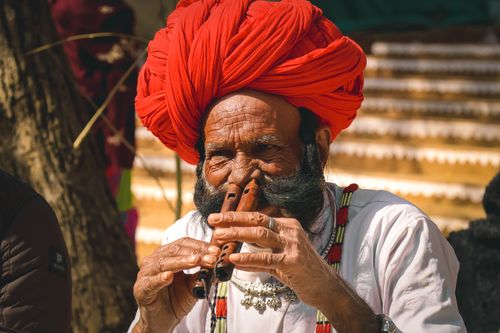 Free A senior man in Udaipur playing a wooden flute, showcasing traditional Rajasthan attire and culture. Stock Photo