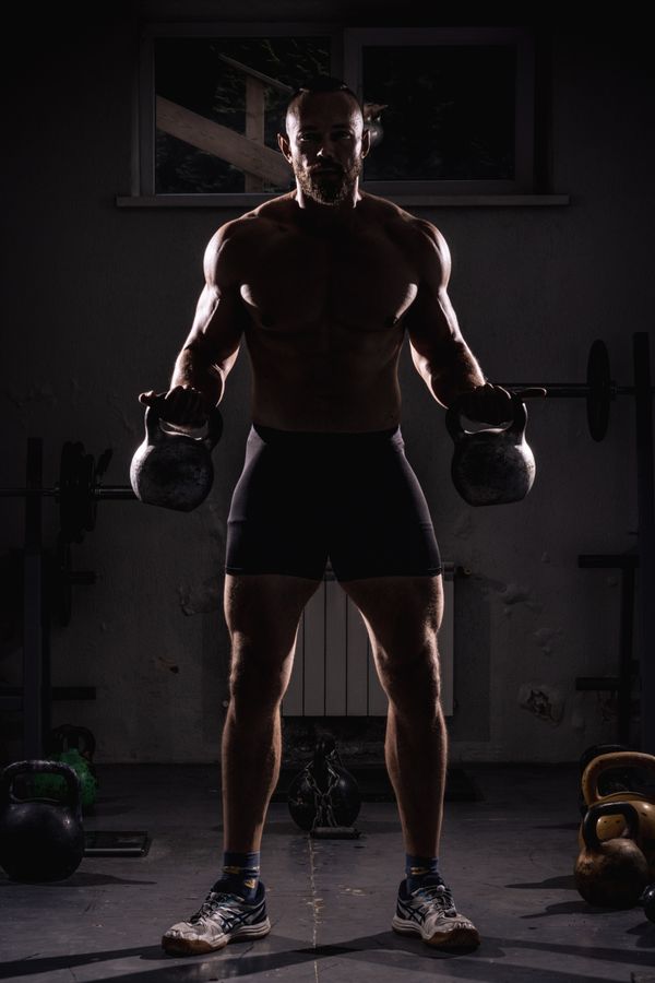 Man lifting kettlebells in dark gym