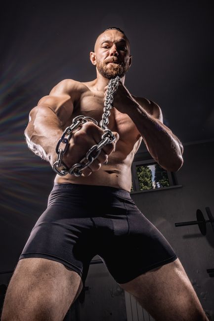 Strong bearded man with chains, showcasing muscles and fitness in gym setting. Strong bearded man with chains, showcasing muscles and fitness in gym setting.