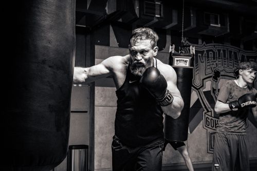Free Powerful image of athletes training in boxing, focusing on a bearded boxer hitting a punching bag indoors. Stock Photo