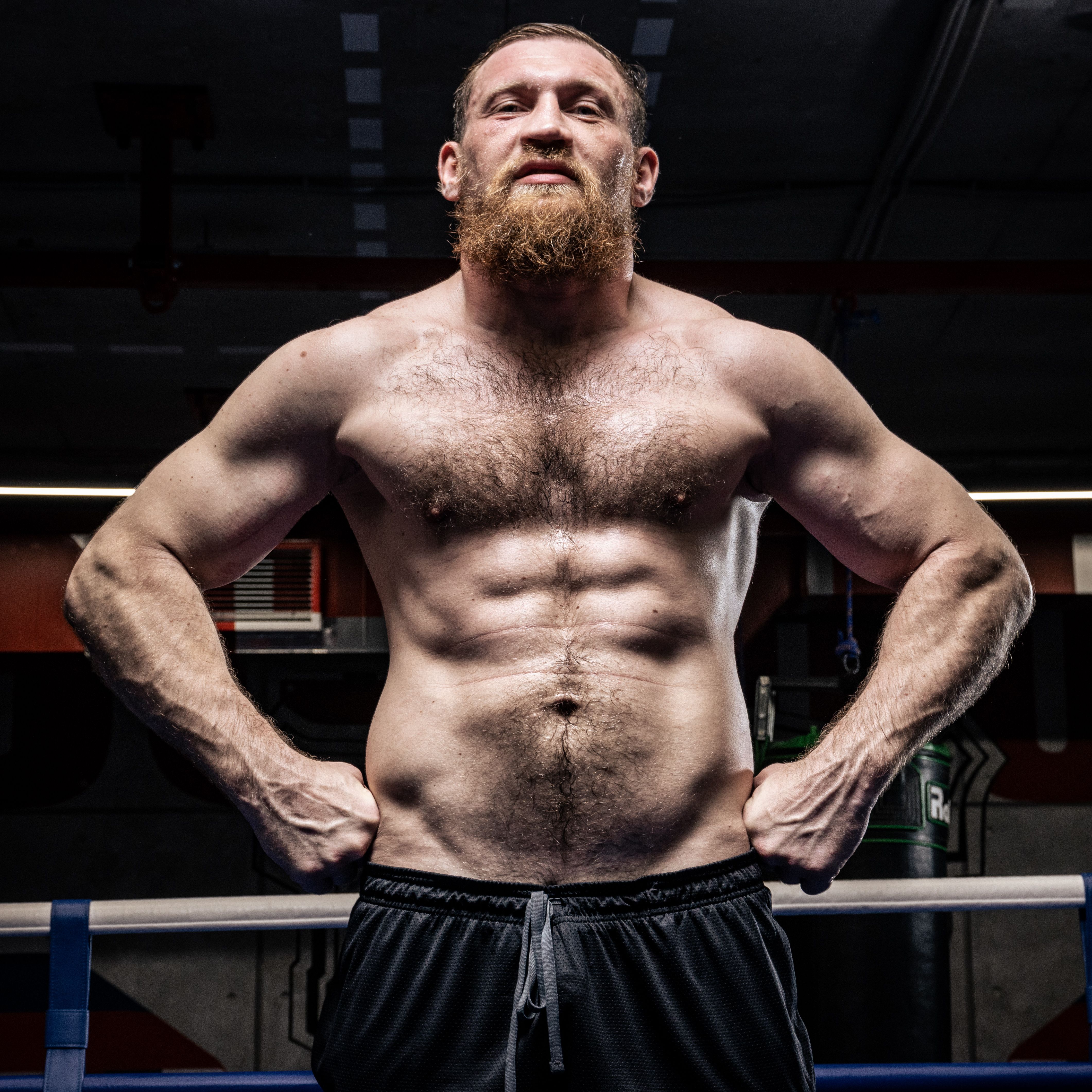 Strong shirtless man with beard displaying muscle definition in a gym setting.