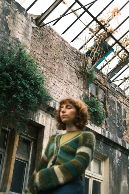 Young woman stands in an overgrown, abandoned structure, conveying mystery and nostalgia.