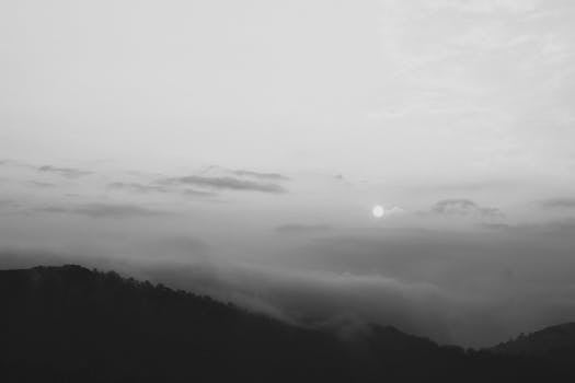 Serene black and white landscape of foggy mountains at dawn with a rising sun.
