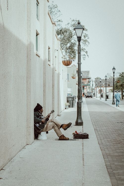 Free A street musician strumming a guitar against a white wall in an urban setting. Stock Photo