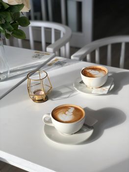 Two cappuccino cups with latte art on a white table, perfect for a cozy cafe vibe.