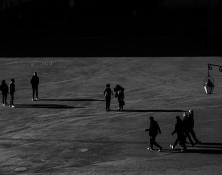 Dramatic black and white photo of people casting long shadows on an open street.