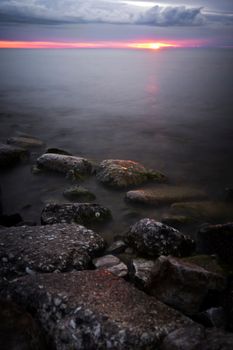 Captivating seascape of Sheboygan, WI, featuring rocks and a vivid sunset horizon over Lake Michigan.