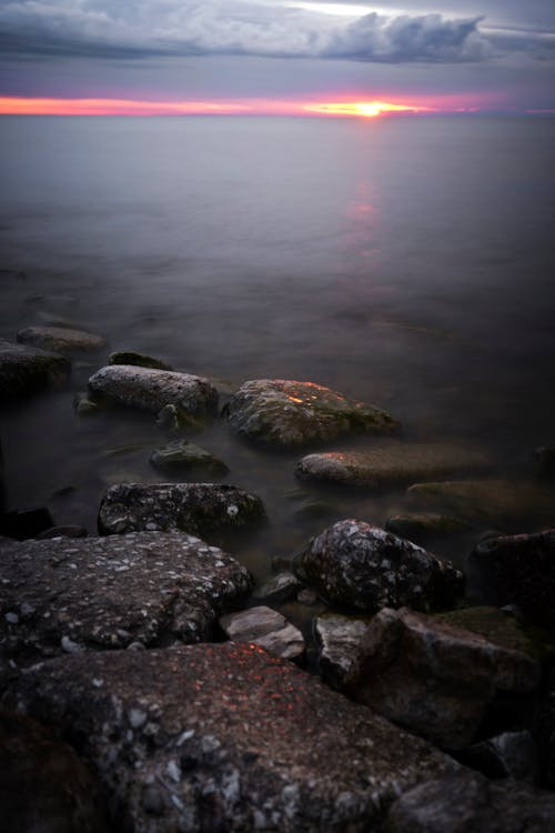 A sunset over the water with rocks and rocks · Free Stock Photo