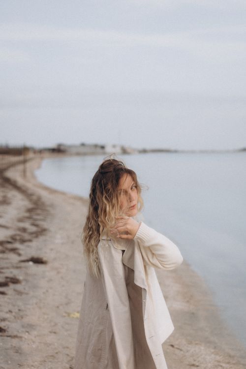 Free A woman standing on Berdiansk beach, looking back with a serene expression against the calm seashore. Stock Photo