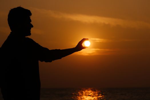 A dramatic silhouette of a person holding the sun during a sunset on Saint Martin beach.