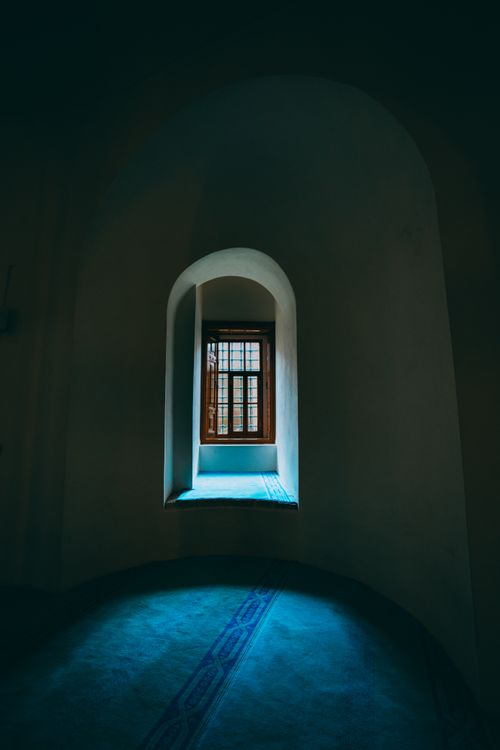 Free Arched window emits soft light in a dark and serene church interior. Stock Photo