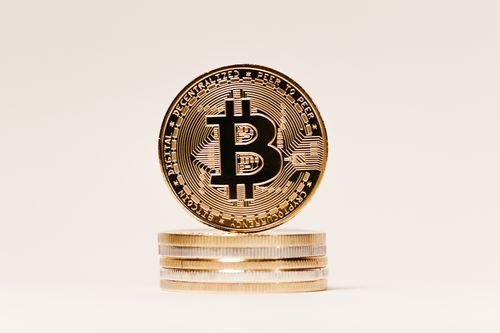Free Close-up of a golden Bitcoin symbol coin on stacked coins with a white background, perfect for finance and technology content. Stock Photo