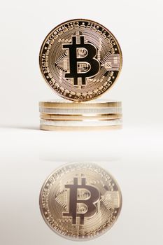 Vertical shot of stacked Bitcoin coins reflecting on a shiny surface.