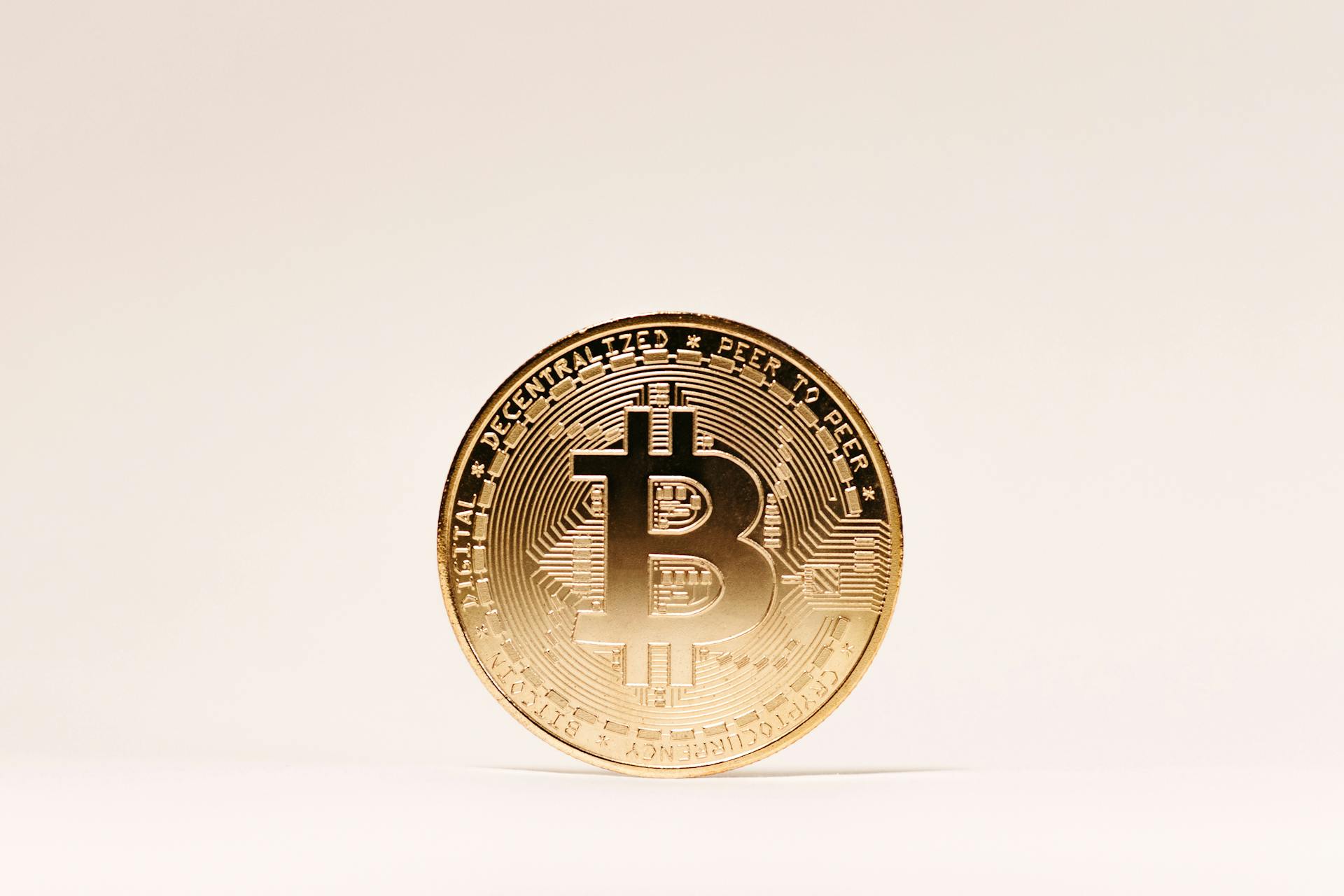 A golden Bitcoin coin standing upright against a minimalist light background.