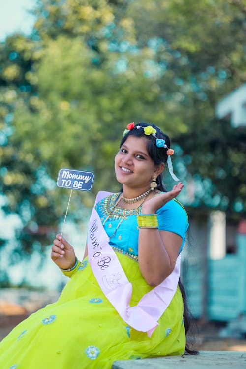 Smiling Pregnant Woman Holding a Placard with Mom To be Message