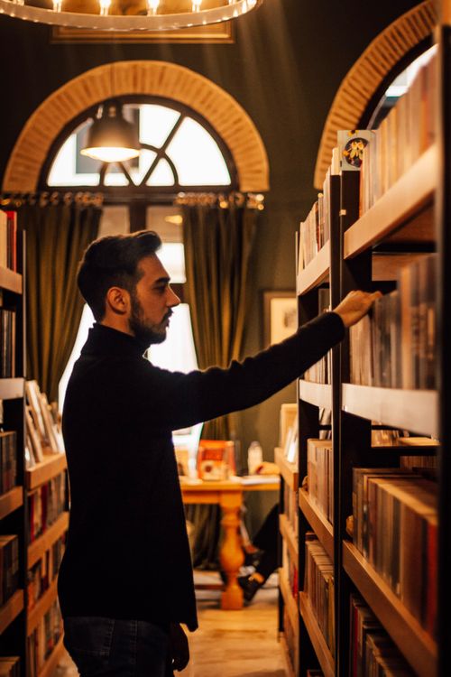 Free A man browsing a bookshelf in a warm, cozy library interior in Adana, Turkey. Stock Photo