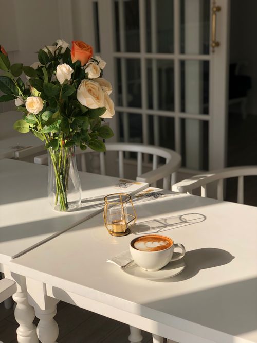 Free Warm and inviting coffee scene with floral arrangement on a white table, ideal for relaxation. Stock Photo