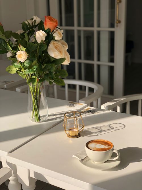 Free A serene morning scene with a bouquet of roses, coffee cup, and candle on a sunlit table. Stock Photo