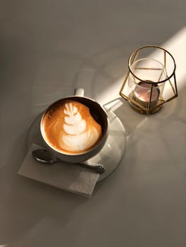 Warm cappuccino with elegant latte art served alongside a lit candle on a sunlit table.
